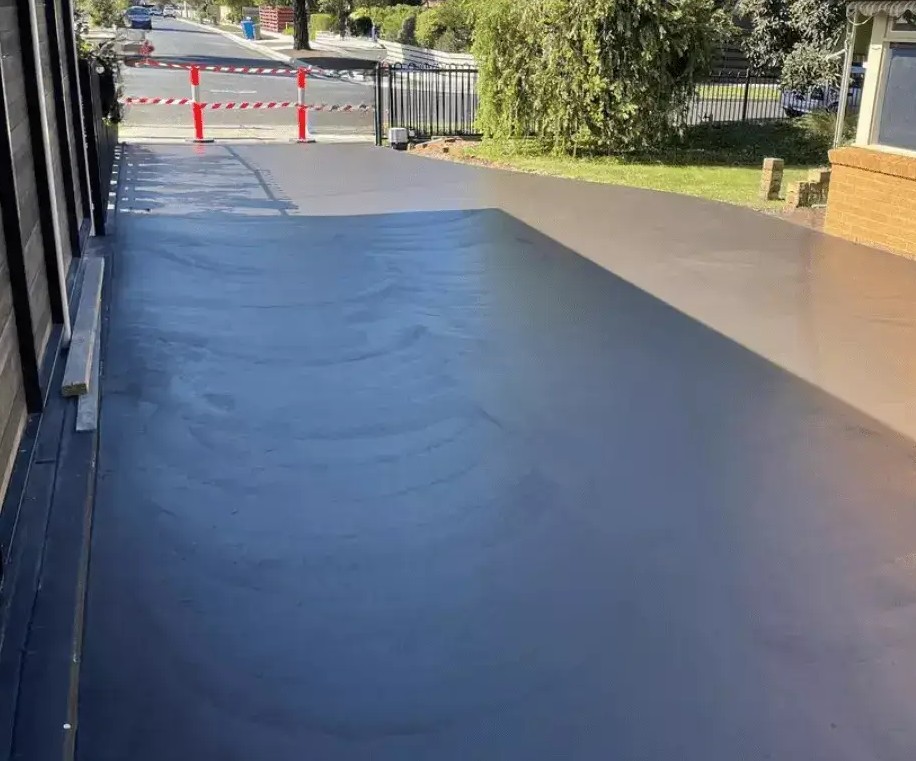 Charcoal coloured concrete driveway between a fence and a building