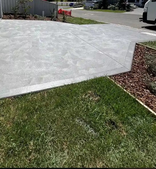 Light toned concrete driveway with saw cut joints beside a lawn
